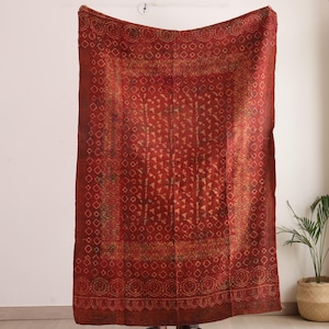 Könnte beinhalten: Ein rechteckiges Textil mit einer tiefroten Grundfarbe und komplexen goldfarbenen geometrischen Mustern. Das Design umfasst ein zentrales Feld mit sich wiederholenden dreieckigen Motiven, umgeben von einer breiten Bordüre aus kreisförmigen und rautenförmigen Elementen.