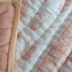 Może przedstawiać: Biała bawełniana kołdra z brzoskwiniową lamówką i wzorem paisley. Kołdra ma kwiatowy wzór na lamówce.