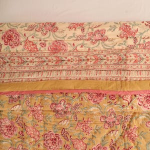 May include: A quilted textile featuring a floral pattern with pink and red blossoms on a cream background, separated by a horizontal mustard yellow band and a thin pink stripe from a lower section with the same floral pattern on a mustard background.