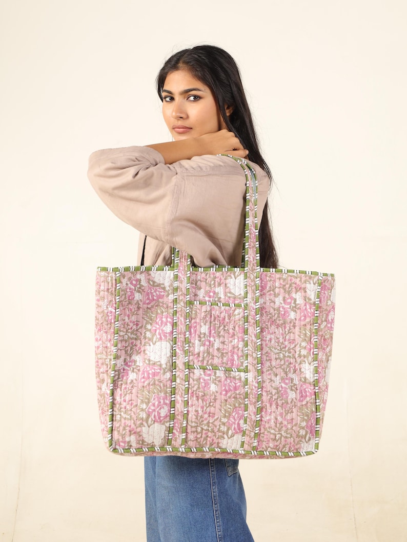 May include: A large pink and green floral tote bag with a quilted design. The bag has a wide base and two long straps.
