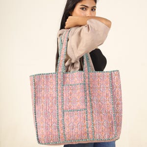 May include: A large pink and blue quilted tote bag with a geometric pattern. The bag has two long handles and a zipper closure.