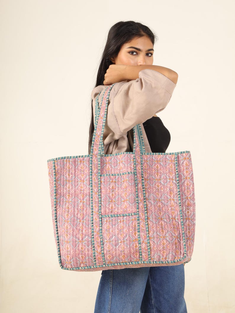 May include: A large pink and blue quilted tote bag with a geometric pattern. The bag has two long handles and a zipper closure.