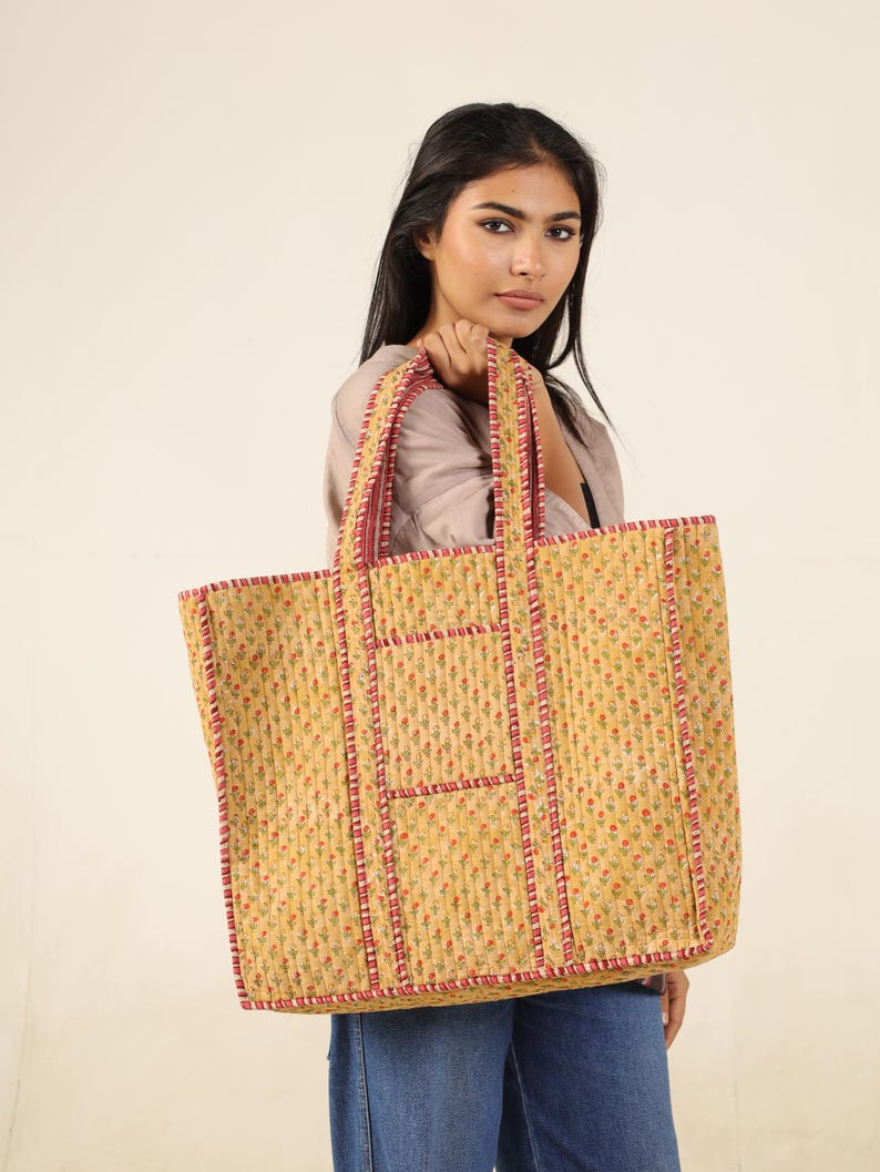 May include: A large yellow tote bag with a floral print and red trim. The bag has multiple pockets and is made of quilted fabric.