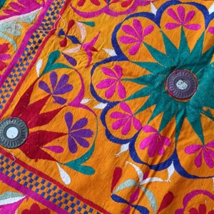 Può includere: Un tessuto arancione vibrante con ricami intricati in tonalità di rosa, viola, verde e blu. Il design presenta motivi floreali e motivi geometrici.