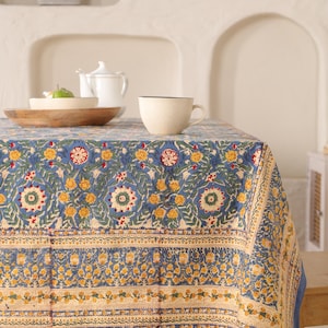 May include: A blue tablecloth with a floral pattern in shades of yellow, red, and green. The tablecloth has a border with a repeating pattern of yellow and white.