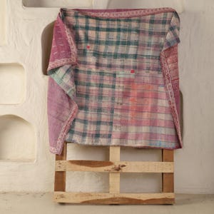 May include: A vintage patchwork quilt with a plaid pattern in shades of pink, green, and white. The quilt is draped over a wooden pallet, showcasing its handmade quality and rustic charm. The edges are finished with a contrasting pink border.