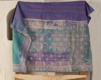 May include: A multi-colored textile with a patchwork design. The top portion is a solid purple, transitioning to a teal and white section, and then a green section. The textile is draped over a wooden structure.