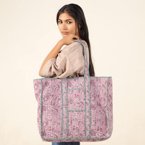 May include: A large pink and green floral tote bag with a quilted design and multiple pockets. The bag has a long strap and is made of cotton.