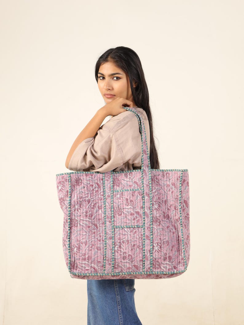 May include: A large pink and green floral tote bag with a quilted design and multiple pockets. The bag has a long strap and is made of cotton.