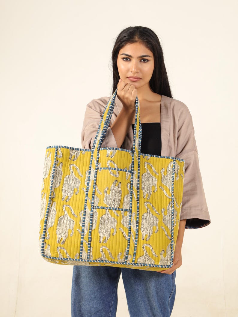 May include: A large yellow tote bag with a blue and white patterned design. The bag has a quilted texture and features a repeating pattern of stylized animals.