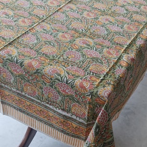 Puede incluir: Un mantel verde con un patrón floral en tonos de amarillo, naranja y rosa. El mantel tiene un borde con un patrón a rayas en amarillo y blanco.