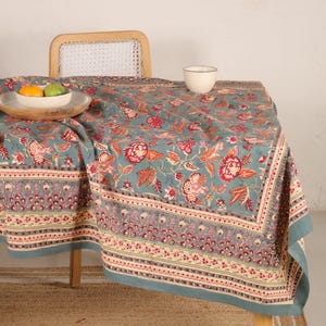 Könnte beinhalten: Eine blaue Tischdecke mit Blumenmuster in Rosa und Orange. Die Tischdecke liegt auf einem Tisch mit einem Stuhl und einer Schale mit Obst.