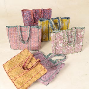 May include: Six quilted tote bags in various floral patterns and colors, including pink, yellow, purple, and green. The bags have a simple design with a single pocket on the front and two handles.