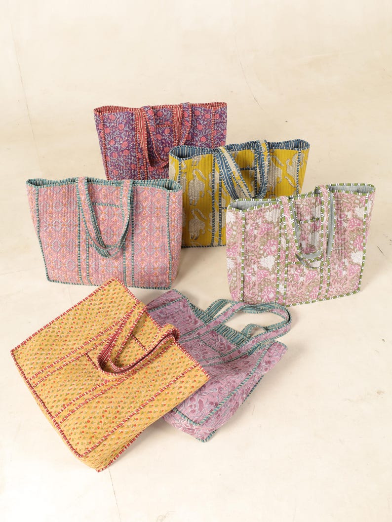 May include: Six quilted tote bags in various floral patterns and colors, including pink, yellow, purple, and green. The bags have a simple design with a single pocket on the front and two handles.