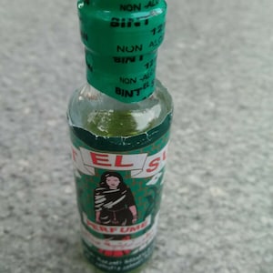 Puede incluir: Una botella de vidrio verde con una tapa blanca y una etiqueta verde. La etiqueta tiene una mujer con un vestido verde y el texto "EL SUR" y "PERFUME". La botella también tiene el texto "NON-ALC" y "BINT" en ella.