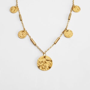 May include: A gold necklace with a hammered metal pendant and smaller hammered metal circles hanging from the chain.