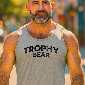 May include: A gray tank top with the words "TROPHY BEAR" printed in black. The tank top is sleeveless and made of a soft material. The person in the image is wearing the tank top.