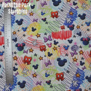 May include: White fabric with a colourful, whimsical pattern featuring Mickey Mouse and Minnie Mouse characters, stars, and scribbled lines. The text "Paint the Park - Scribbles" is at the top of the fabric.