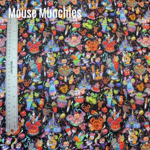 Puede incluir: Tela negra con un patrón colorido de personajes de dibujos animados, postres y castillos. El texto "Mouse Munchies" está en la parte superior. Una regla muestra medidas en centímetros.