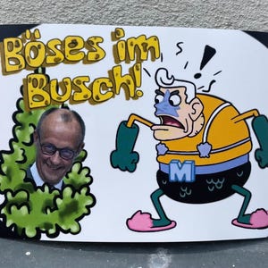 Könnte beinhalten: Ein weißer Aufkleber mit dem deutschen Text "Böses im Busch!" in gelben Buchstaben. Der Aufkleber zeigt eine Zeichentrickfigur in einem gelb-blauen Kostüm und das Gesicht eines Mannes, der aus einem grünen Busch lugt.