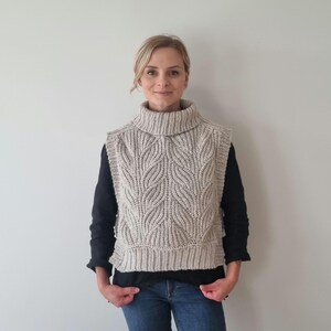 May include: A beige crocheted vest with a turtleneck collar and a leaf pattern. The vest is sleeveless and has a cropped length.
