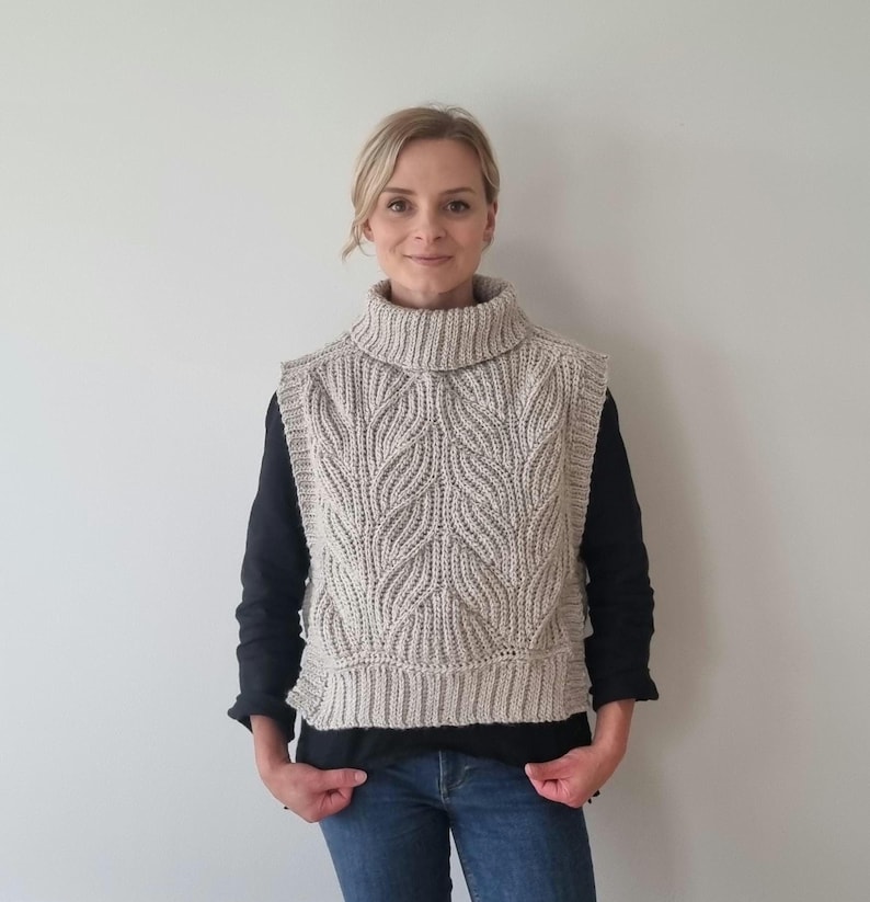 May include: A beige crocheted vest with a turtleneck collar and a leaf pattern. The vest is sleeveless and has a cropped length.