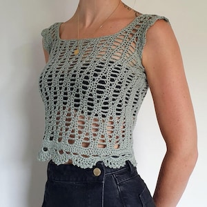 Könnte beinhalten: Ein salbeigrünes Häkeltop mit quadratischem Ausschnitt und kurzen Ärmeln. Das offene Webmuster gibt einen Blick auf die darunterliegende Unterwäsche frei. Der untere Saum hat einen gewellten Rand. Der Text "@BdBs_KnitKnots" ist unten sichtbar.