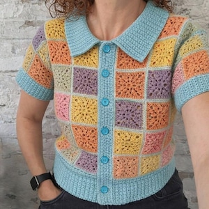Può includere: Top all'uncinetto a maniche corte e colorato, con colletto e finiture azzurre. Il top presenta un design patchwork nei toni dell'arancione, giallo, rosa e viola, con bottoni azzurri sul davanti. Capo fatto a mano.
