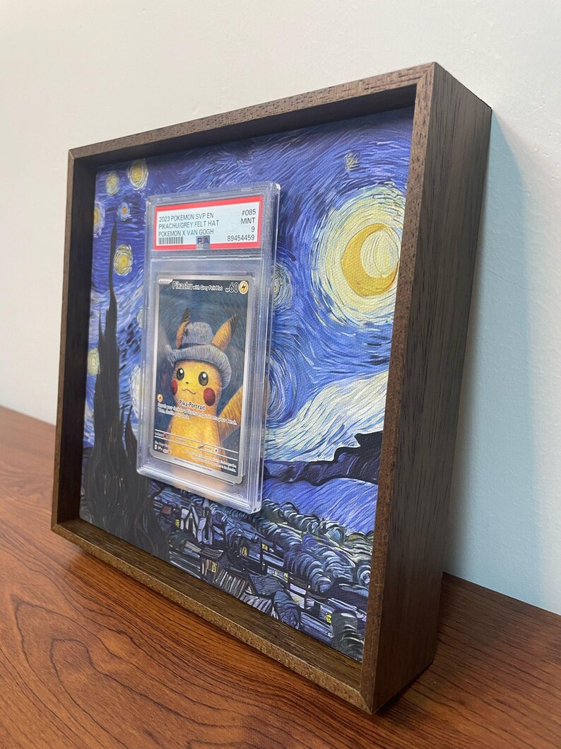 May include: A framed print of Vincent van Gogh's Starry Night with a graded Pokemon card featuring Pikachu wearing a grey felt hat in the center. The card is graded a 9 and is labeled "#005 MINT".