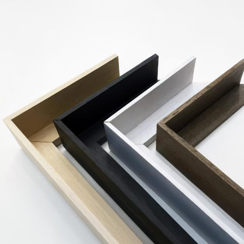 May include: Four different picture frames, each with a different color and wood grain. The frames are stacked on top of each other, with the lightest frame on the bottom and the darkest frame on top. The frames are all made of wood and have a simple, modern design.