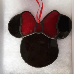 May include: A stained glass ornament shaped like Mickey Mouse's head with a red bow. The ornament is black and red.