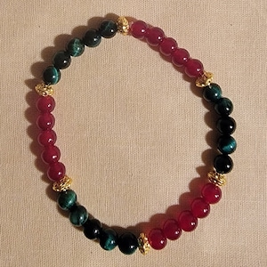 May include: A red and green beaded bracelet with gold accents. The bracelet is made of round beads and has a simple design.