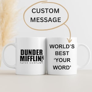 May include: Two white ceramic mugs with black text. The mug on the left has the text "Dunder Mifflin, Inc. Paper Company". The mug on the right has the text "World's Best 'Your Word'".
