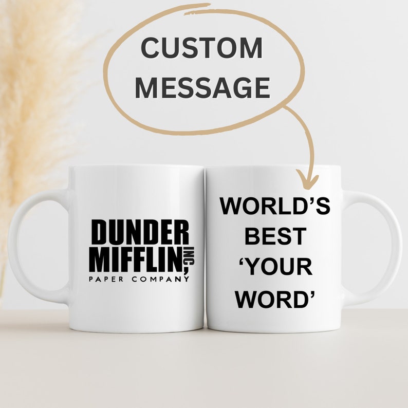 May include: Two white ceramic mugs with black text. The mug on the left has the text "Dunder Mifflin, Inc. Paper Company". The mug on the right has the text "World's Best 'Your Word'".