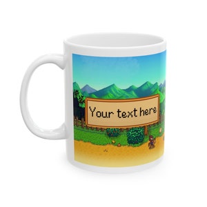 May include: White ceramic mug featuring a pixelated image of a farm scene from a video game. The image depicts a green field, mountains in the background, and a sign that reads "Your text here".