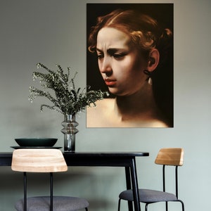 May include: A black and white portrait of a woman with a pearl earring hanging from her ear. The portrait is framed and hanging on a green wall in a dining room setting. A black table with two chairs is in the foreground.
