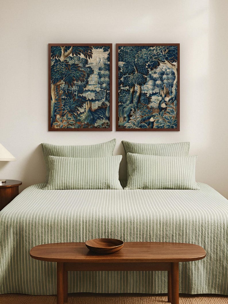 A pair of vintage verdure tapestry prints in warm wood frames hangs above a bed dressed in sage green linens. The blue botanical artwork adds calm, historic charm and creates an elegant focal point in the bedroom wall art arrangement.