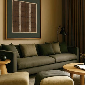 Large vintage textile wall art print with brown and cream woven patterns, displayed above a dark olive green sofa in a modern living room.
