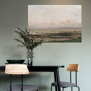 May include: A black dining table with a wood top and two black metal chairs with gray cushions. A painting of a seascape hangs on the wall behind the table.