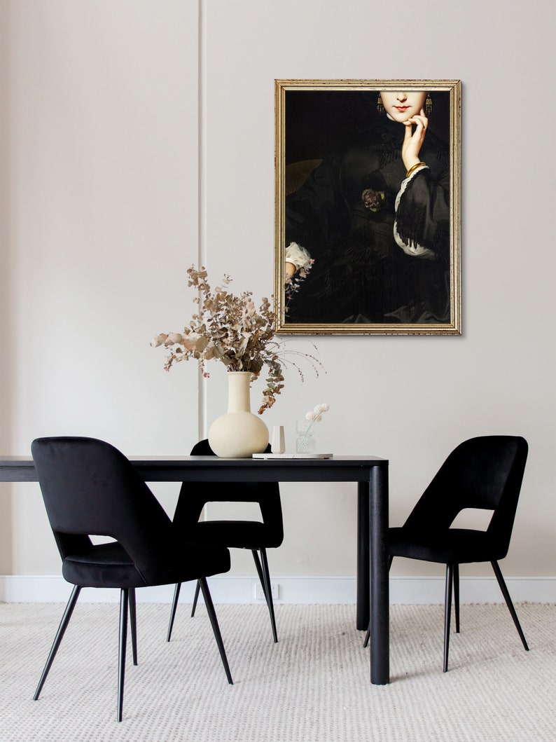 May include: A black framed painting of a woman in a black dress with a gold bracelet on her wrist. The painting is hanging on a white wall above a black dining table with two black velvet chairs.