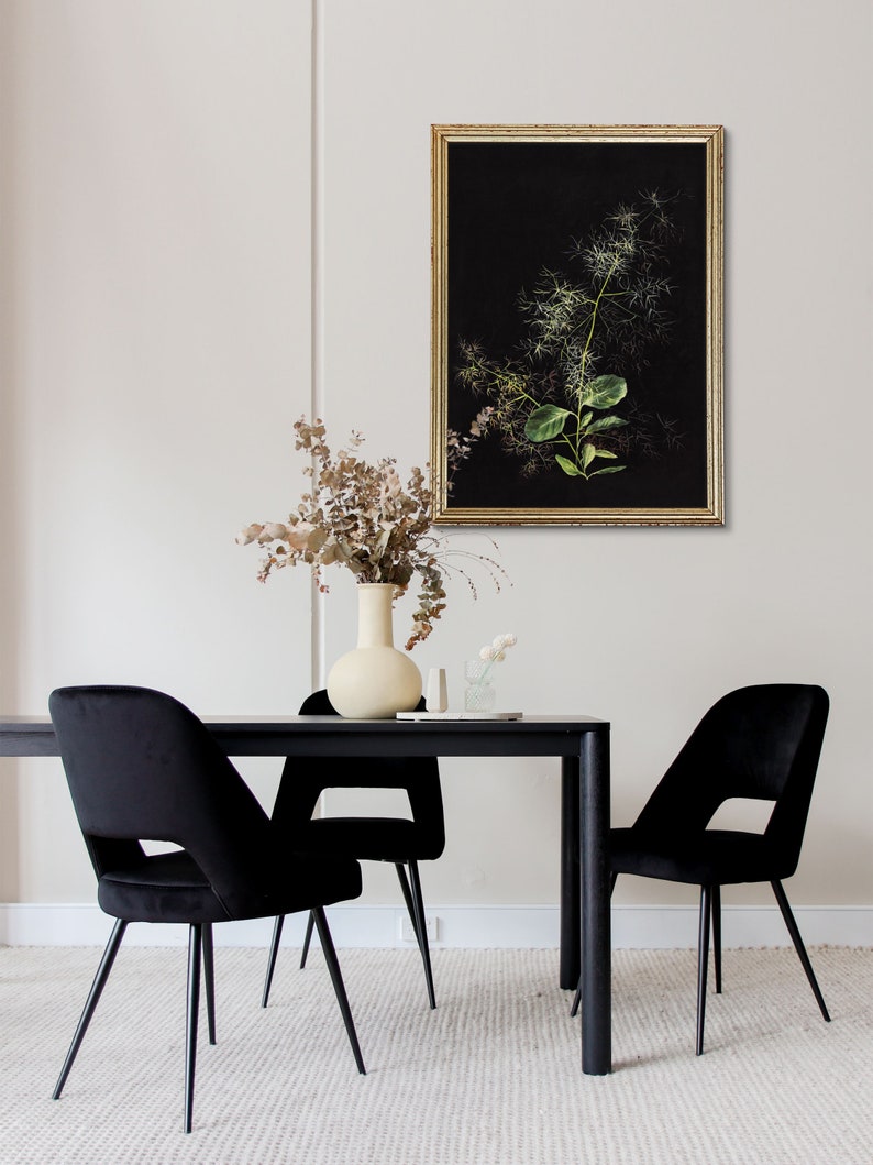 May include: A black dining table with four black velvet chairs. A vase with dried flowers sits on the table, and a framed botanical print hangs on the wall behind the table.