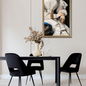 Modern dining room with a black wooden table and black chairs, behind the wall hangs an antique golden frame with an altered art print of a woman.
