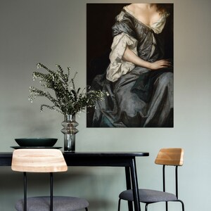 Baroque portrait wall art displayed above a minimalist dining table with greenery in a glass vase. The soft sage green wall and muted colors create a refined, calming interior aesthetic.
