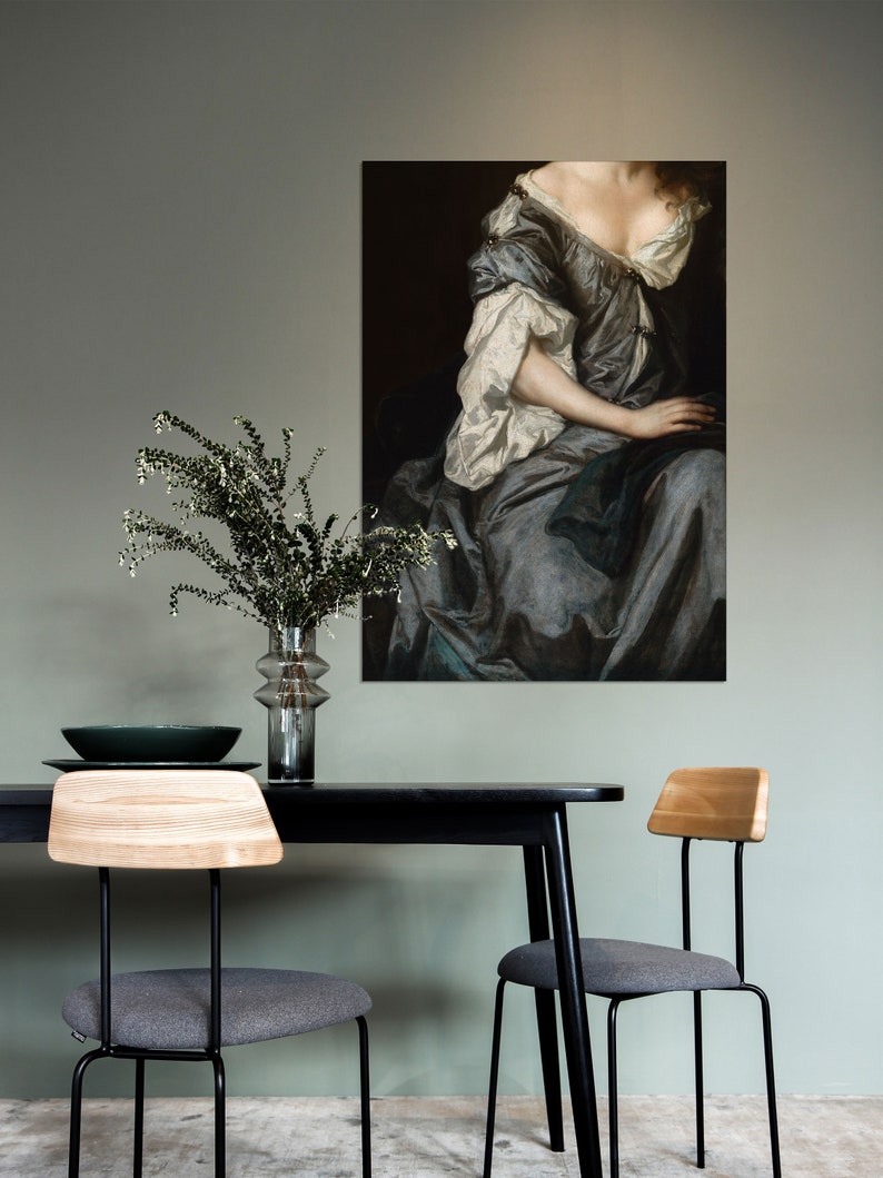Baroque portrait wall art displayed above a minimalist dining table with greenery in a glass vase. The soft sage green wall and muted colors create a refined, calming interior aesthetic.