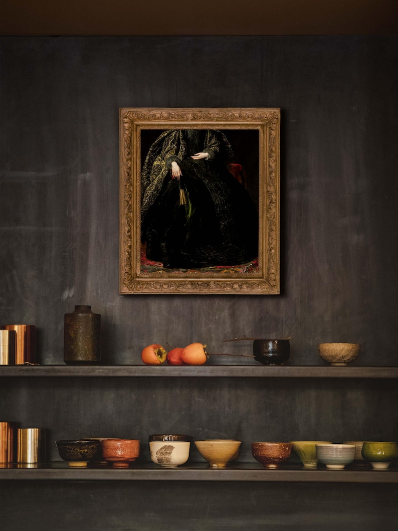 A framed portrait of a woman in a black and gold gown displayed on a dark, moody kitchen wall. Below the artwork, shelves hold a collection of ceramic bowls and decorative objects, enhancing the room's vintage and dark academia-inspired decor