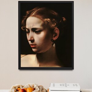 May include: A framed painting of a woman's face. The woman has light brown hair and is wearing a pearl earring. The painting is set against a dark background.