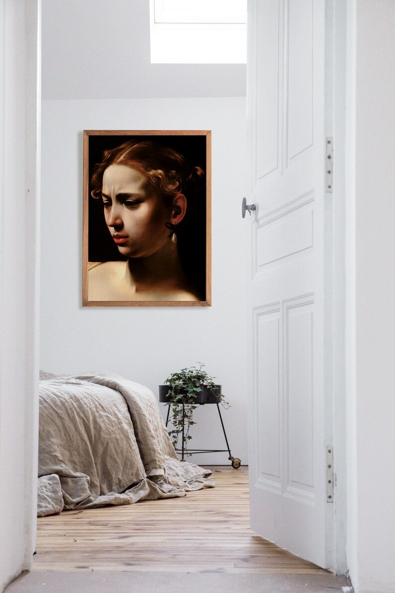 May include: A framed portrait of a woman with dark hair and a pearl earring. The woman is looking down and has a serious expression on her face. The portrait is hanging on a white wall in a room with a wooden floor.