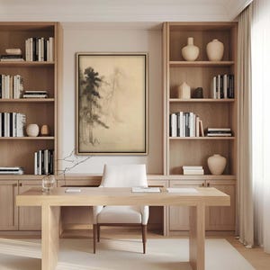 Elegant framed ink landscape print in a home office with built-in wooden shelves. The minimal Japanese painting of misty pine trees complements the natural tones of the Japandi-style decor.