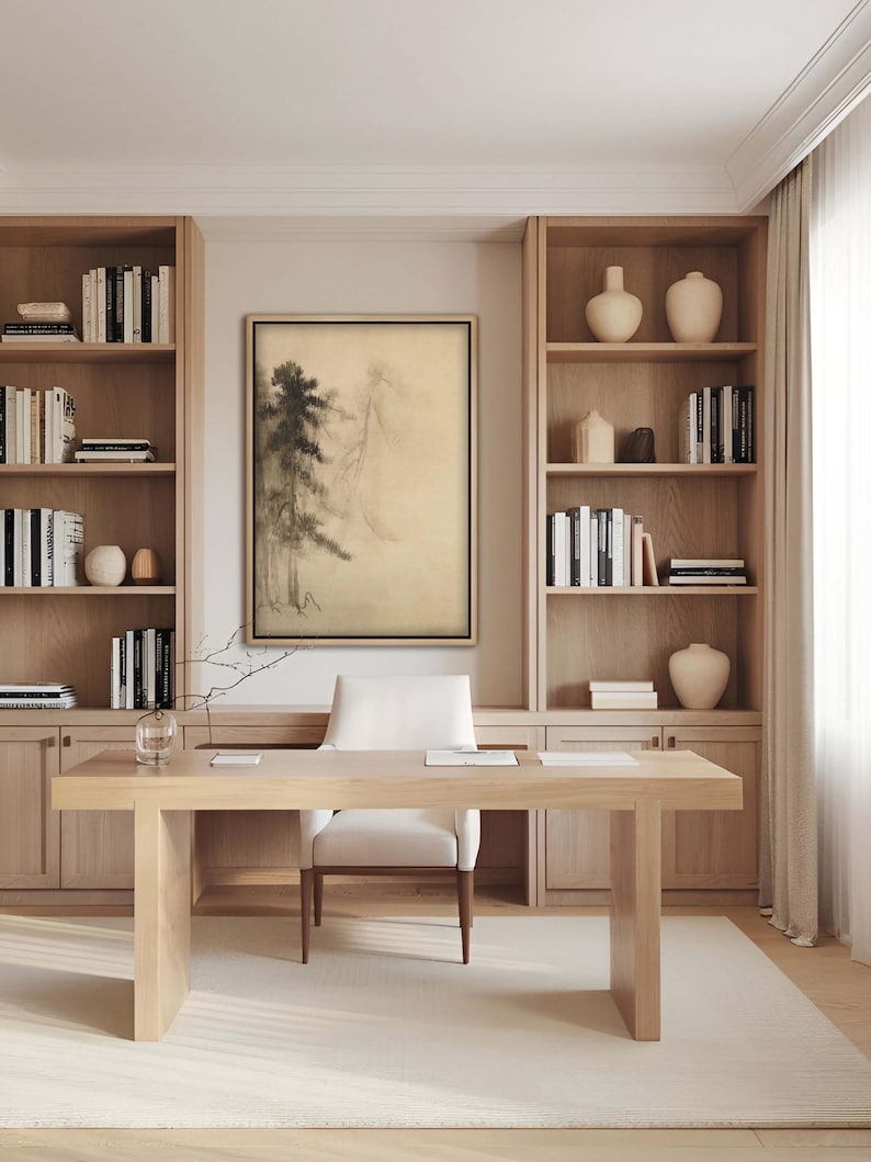 Elegant framed ink landscape print in a home office with built-in wooden shelves. The minimal Japanese painting of misty pine trees complements the natural tones of the Japandi-style decor.