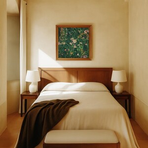 Framed wildflower meadow painting hanging above a wooden bed in a serene, minimalist bedroom with warm beige walls, white bedding, and soft natural light.